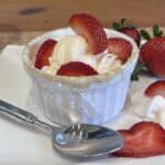 Protein strawberry shortcake mug cake topped with whipped cream, vanilla ice cream, and fresh strawberries in a white ramekin