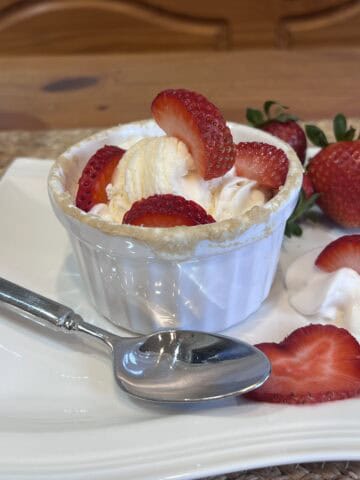 Protein strawberry shortcake mug cake topped with whipped cream, vanilla ice cream, and fresh strawberries in a white ramekin