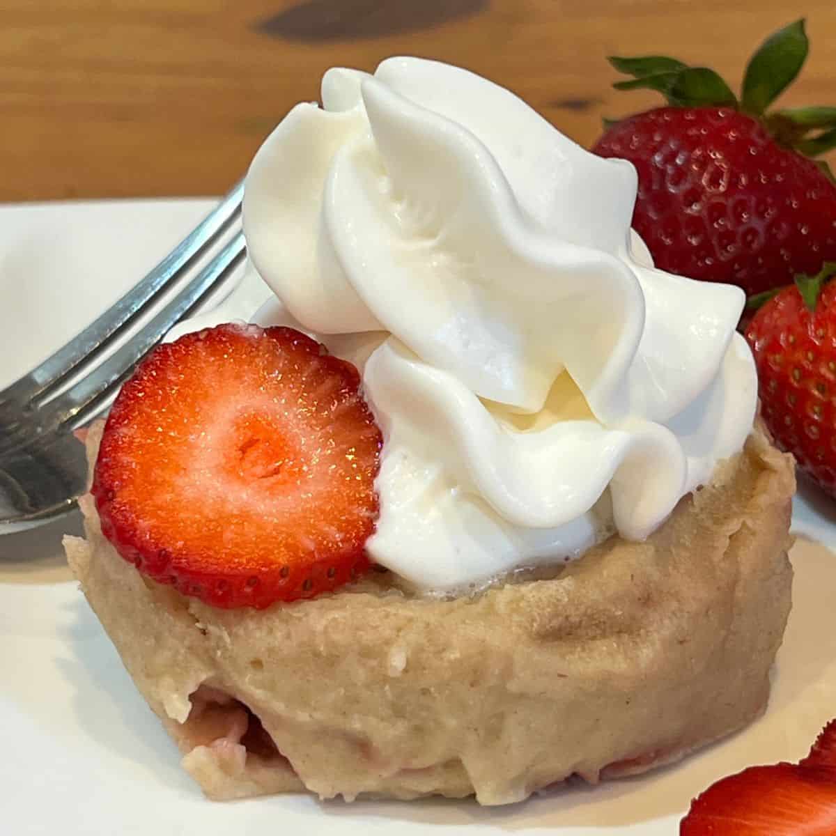Strawberry shortcake mug cake served on a plate with fresh strawberries and whipped cream