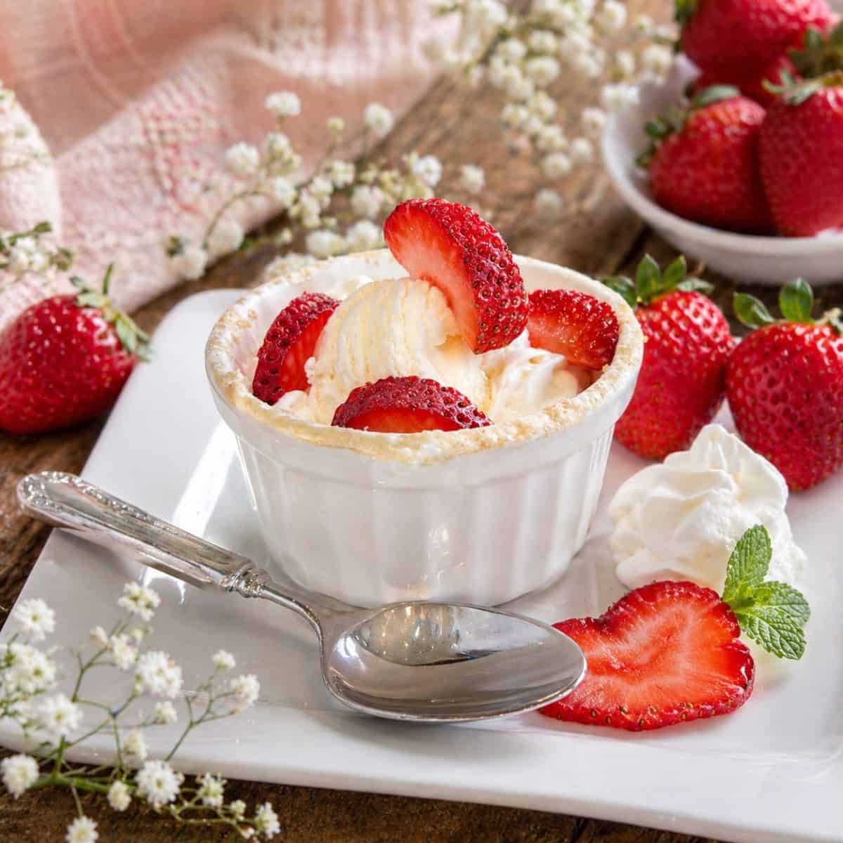 Close up of strawberry shortcake mug cake with fresh strawberries and whipped cream