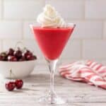 High-protein cherry Jell-O fluff made with Greek yogurt served in a martini glass and topped with whipped cream.