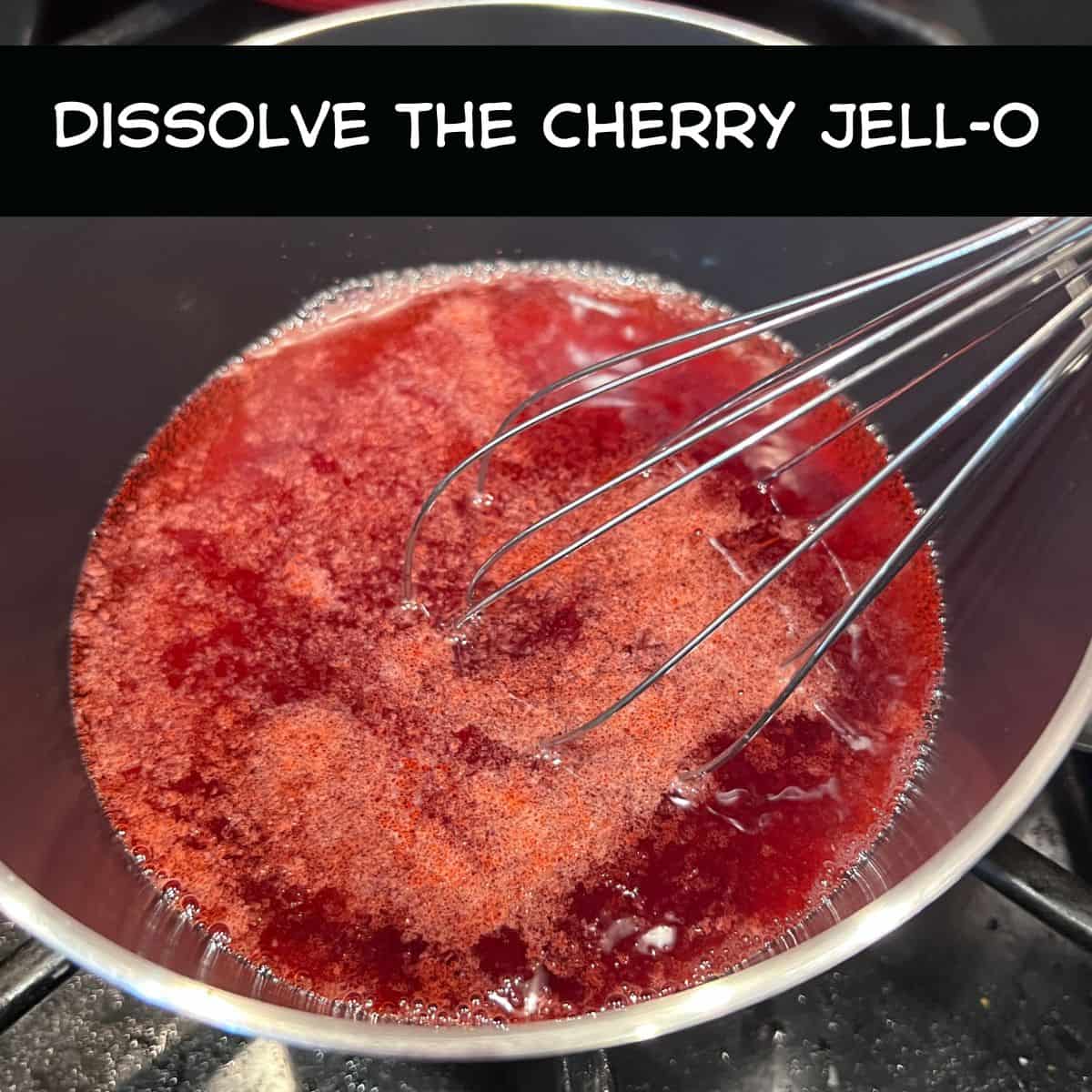 Cherry gelatin dessert mix being whisked into hot water in a saucepan to make high-protein cherry Jell-O fluff.