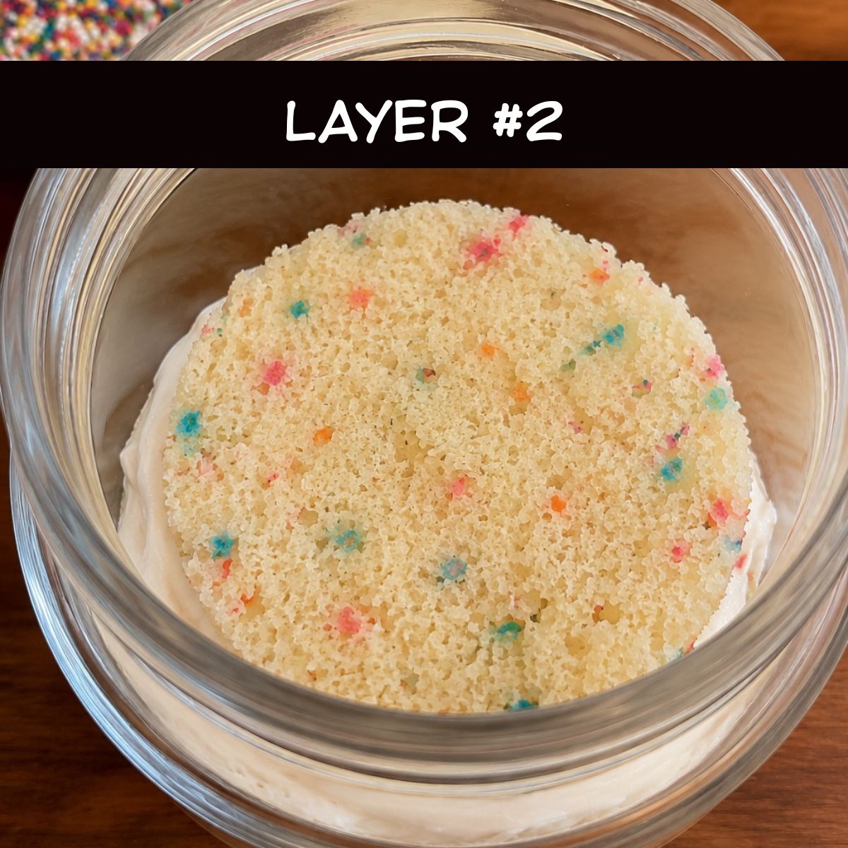 Second Funfetti cake layer placed on top of a frosting layer inside a glass jar while assembling Healthy Funfetti Dot Cake Jars.