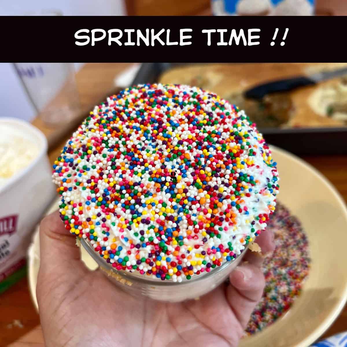 Hand holding a Healthy Funfetti Dot Cake Jar with the frosted top completely coated in rainbow nonpareil sprinkles.