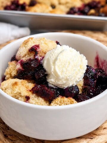 Close-up of an easy 5-ingredient blueberry cobbler served warm in a small white bowl with a scoop of vanilla ice cream melting on top.