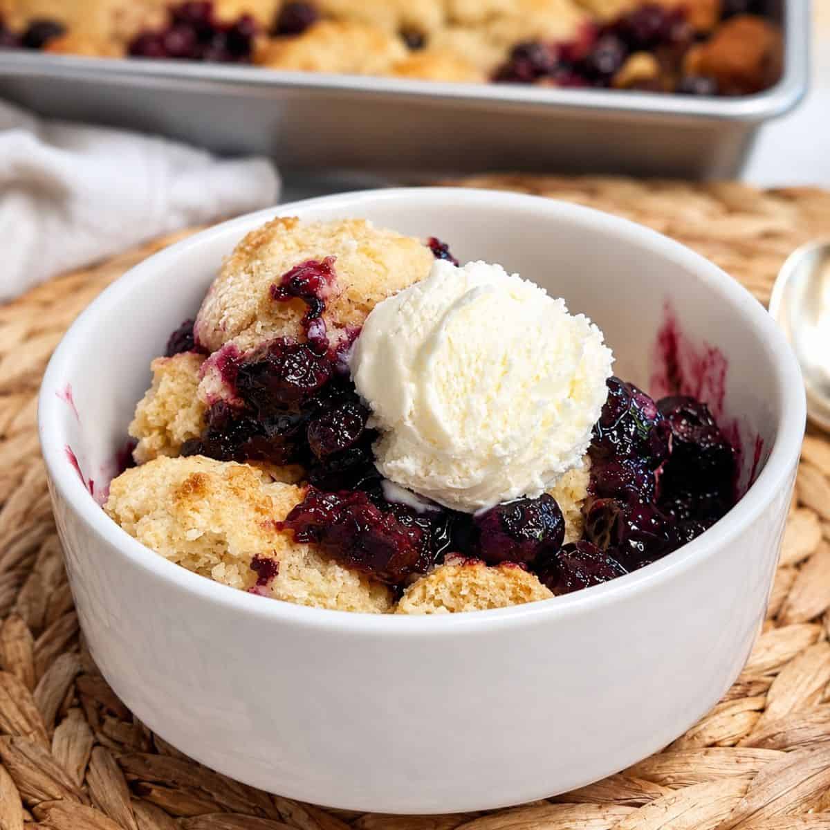 Close-up of an easy 5-ingredient blueberry cobbler served warm in a small white bowl with a scoop of vanilla ice cream melting on top.