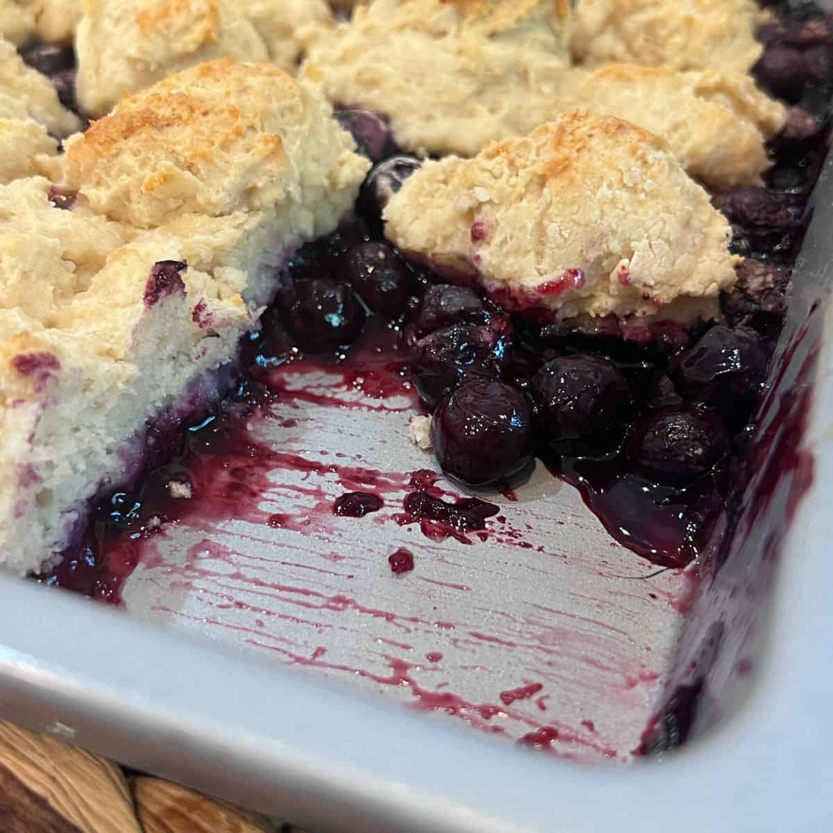 Easy simple Ingredient Shortcut Blueberry Cobbler fresh from the oven with one slice removed, revealing a juicy blueberry filling and golden brown cobbler topping.