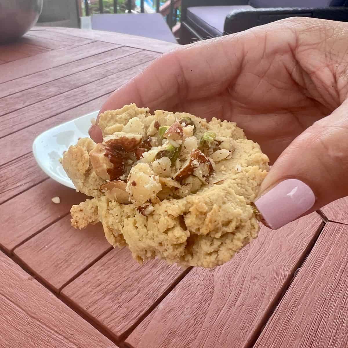 Close-up of a finished Almond Flour Butter Cookie topped with chopped pecans and held in one hand.