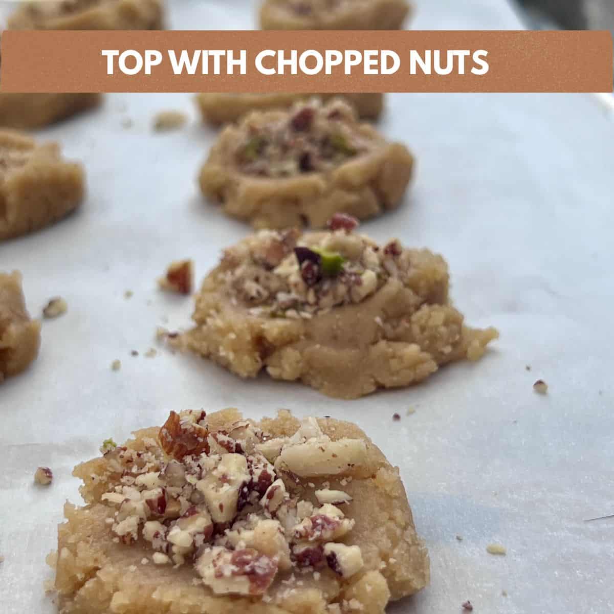 Flattened Almond Flour Butter Cookies topped with chopped pecans on a parchment-lined baking sheet before baking.