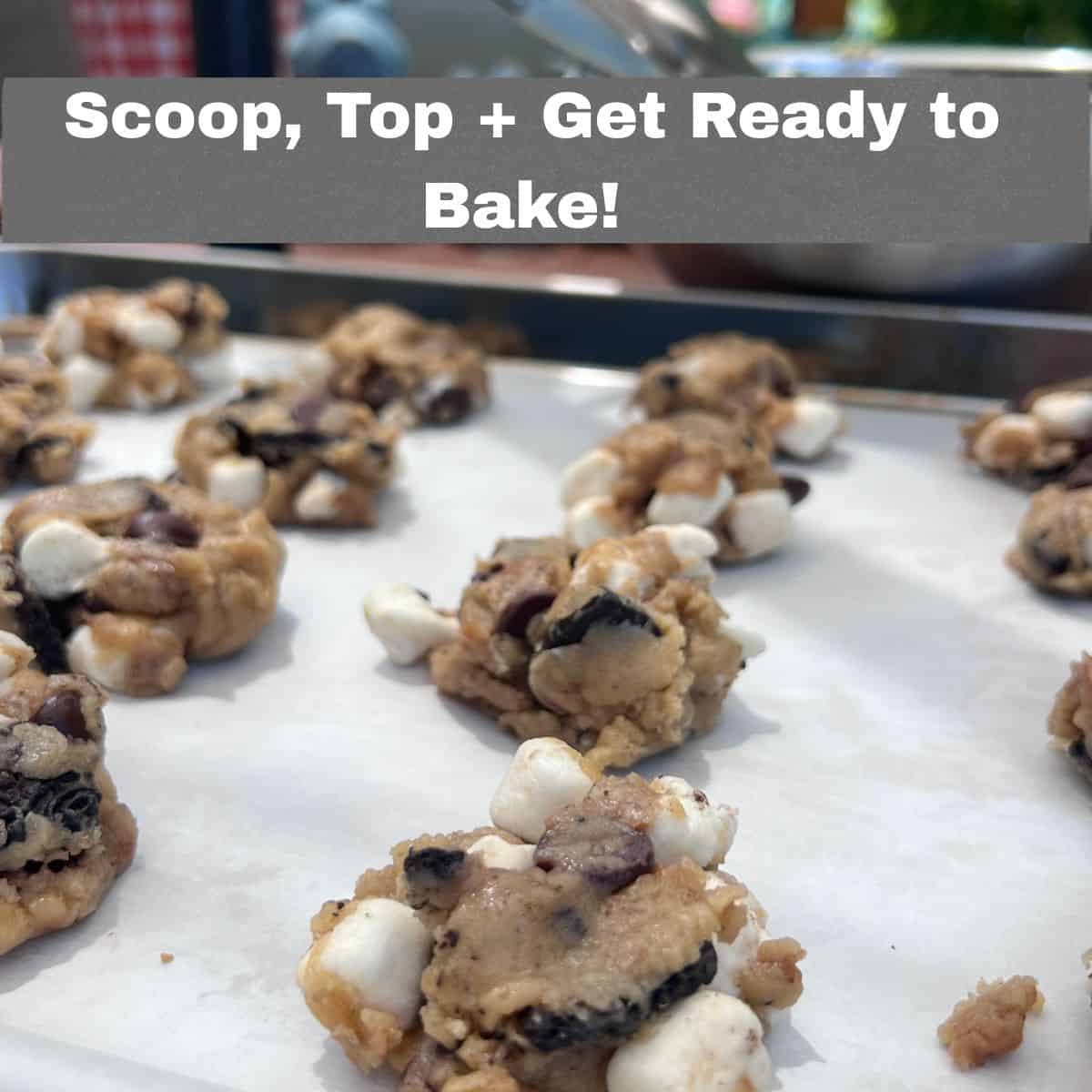 Unbaked Oreo chocolate chip marshmallow cookies topped with Oreo pieces, chocolate chips, and mini marshmallows on a baking sheet