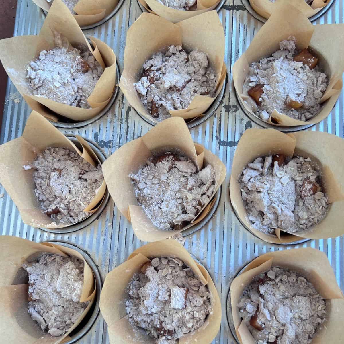 Healthy apple fritter muffins topped with cinnamon apples and oat streusel before baking