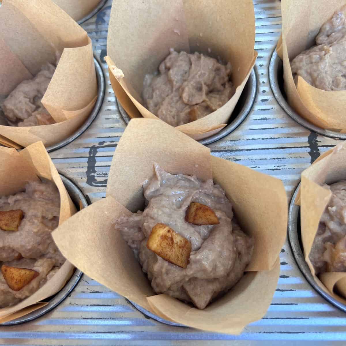 Muffin liners filled with healthy apple fritter muffin batter
