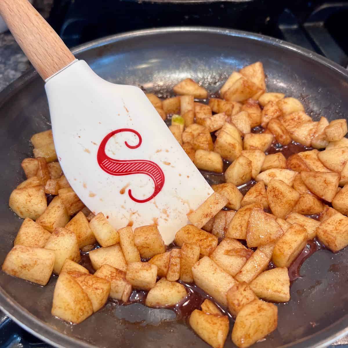 Diced apples cooking with maple syrup and cinnamon in a skillet