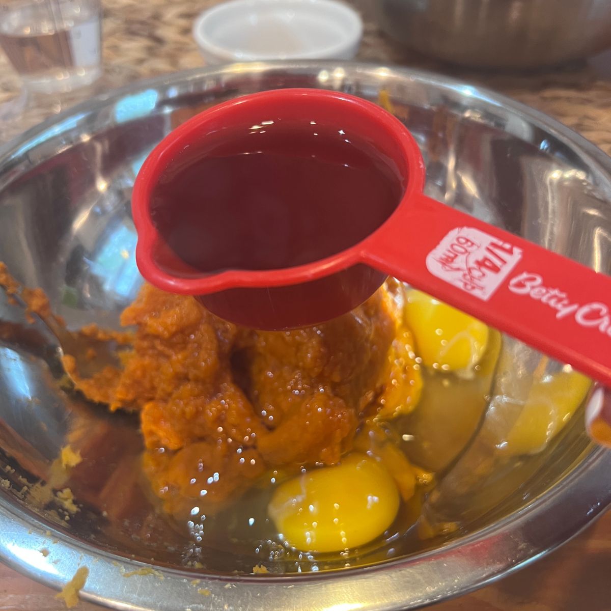 Maple syrup being added to pumpkin puree and eggs for pumpkin sweet potato muffins