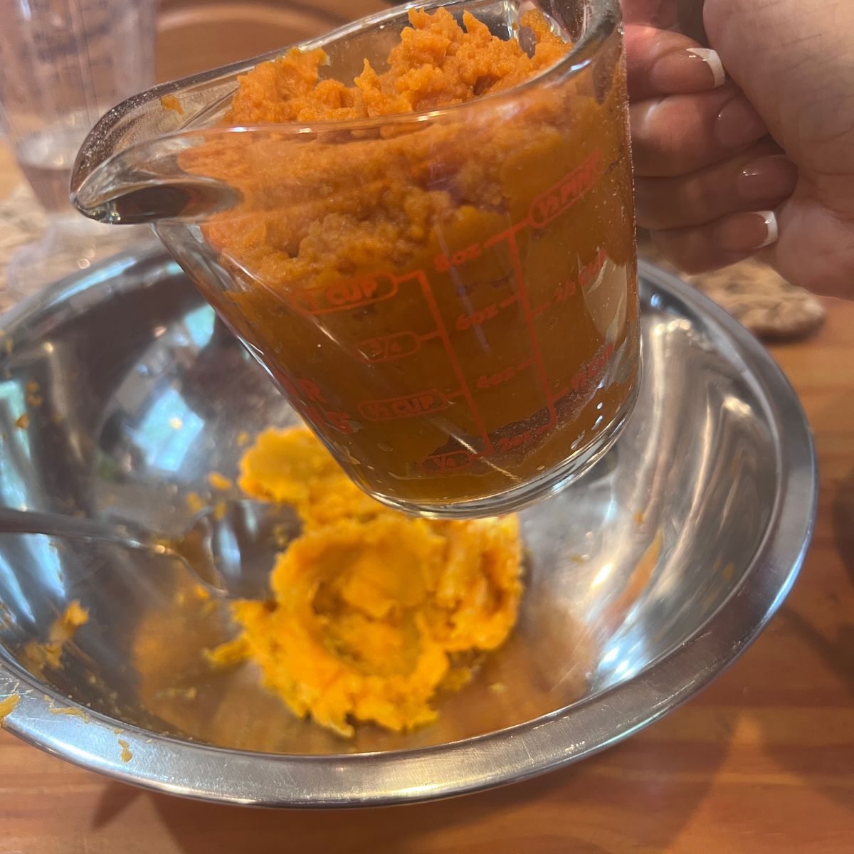 Mashed sweet potato being poured from a glass measuring cup into a mixing bowl