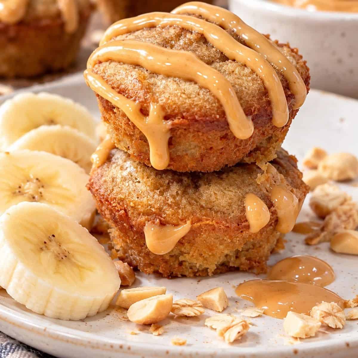 Two stacked 3-ingredient peanut butter banana mini muffins topped with creamy peanut butter drizzle.