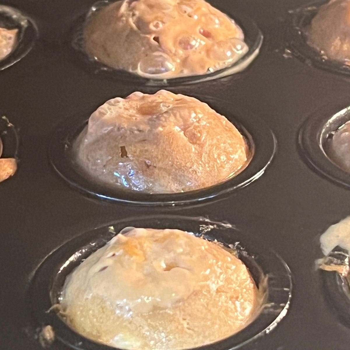 Close-up of flourless peanut butter banana mini muffins rising into golden, puffy little muffins while baking in the oven.