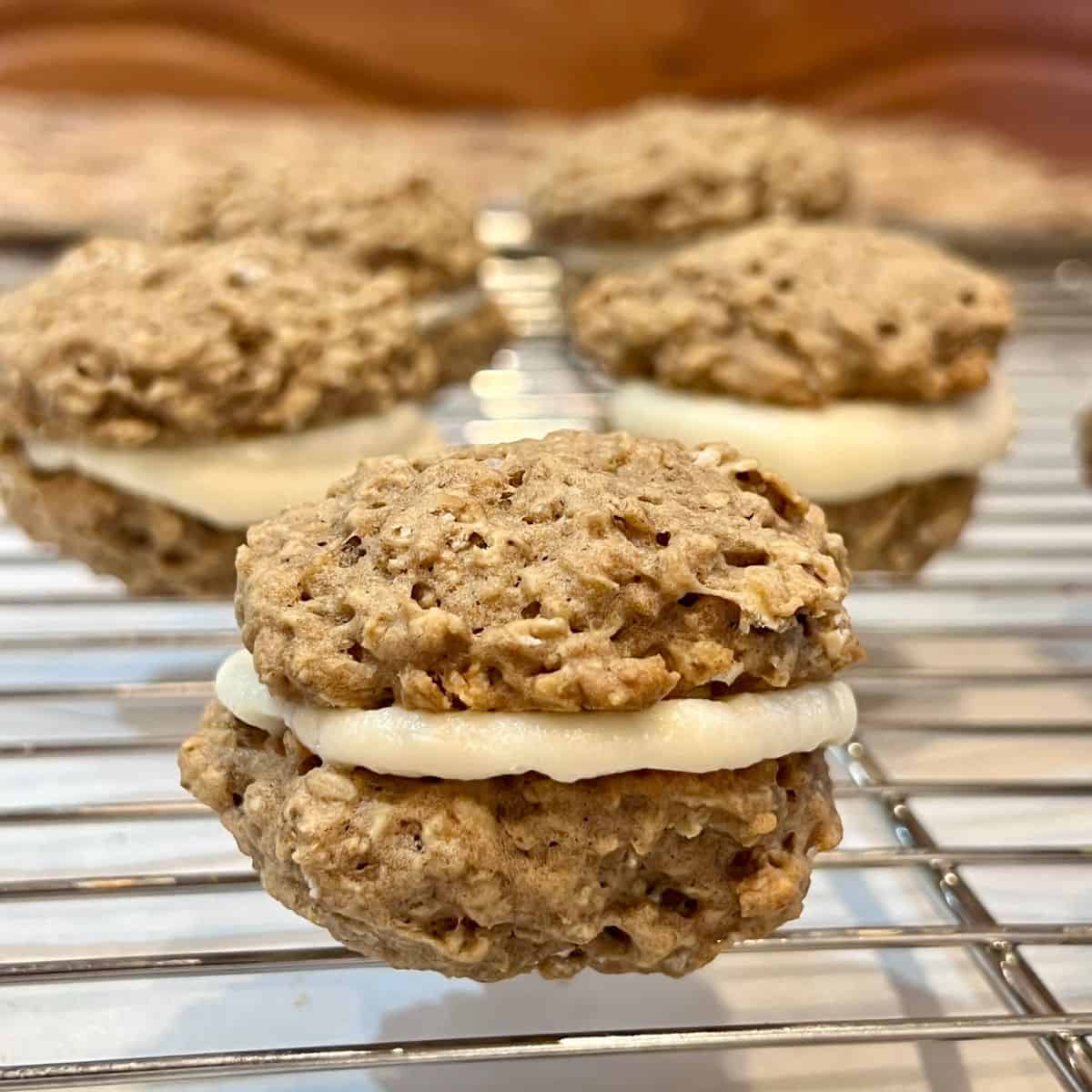 Homemade oatmeal cream pie sandwich cookies with marshmallow cream filling arranged on a wire cooling rack.