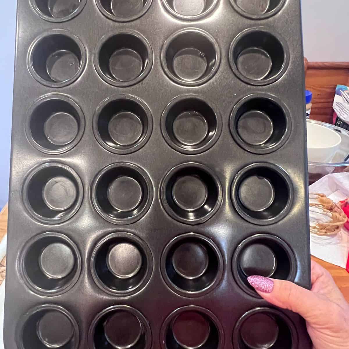 Hand holding a mini muffin pan used to make 3-ingredient peanut butter banana mini muffins without flour.