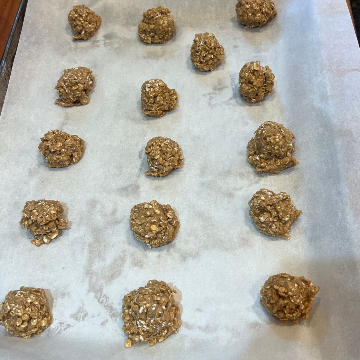 16 oatmeal cream pie cookie dough balls arranged on a parchment-lined baking sheet, ready to be baked.
