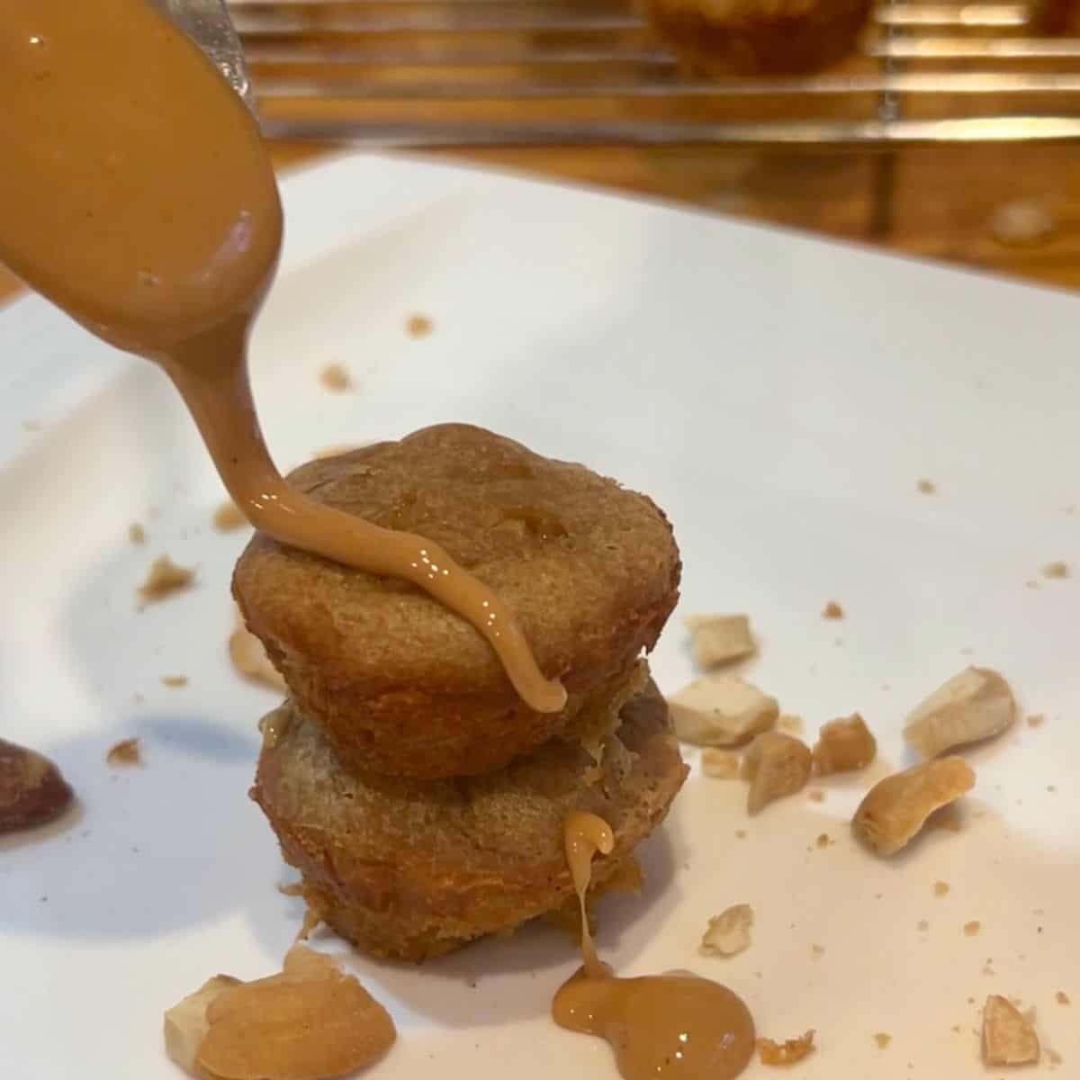 Close-up of a spoon drizzling creamy peanut butter over a homemade 3-ingredient peanut butter banana mini muffin.